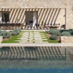 Fachada de piedra con sombras de pérgola y camino de losas que lleva a la piscina