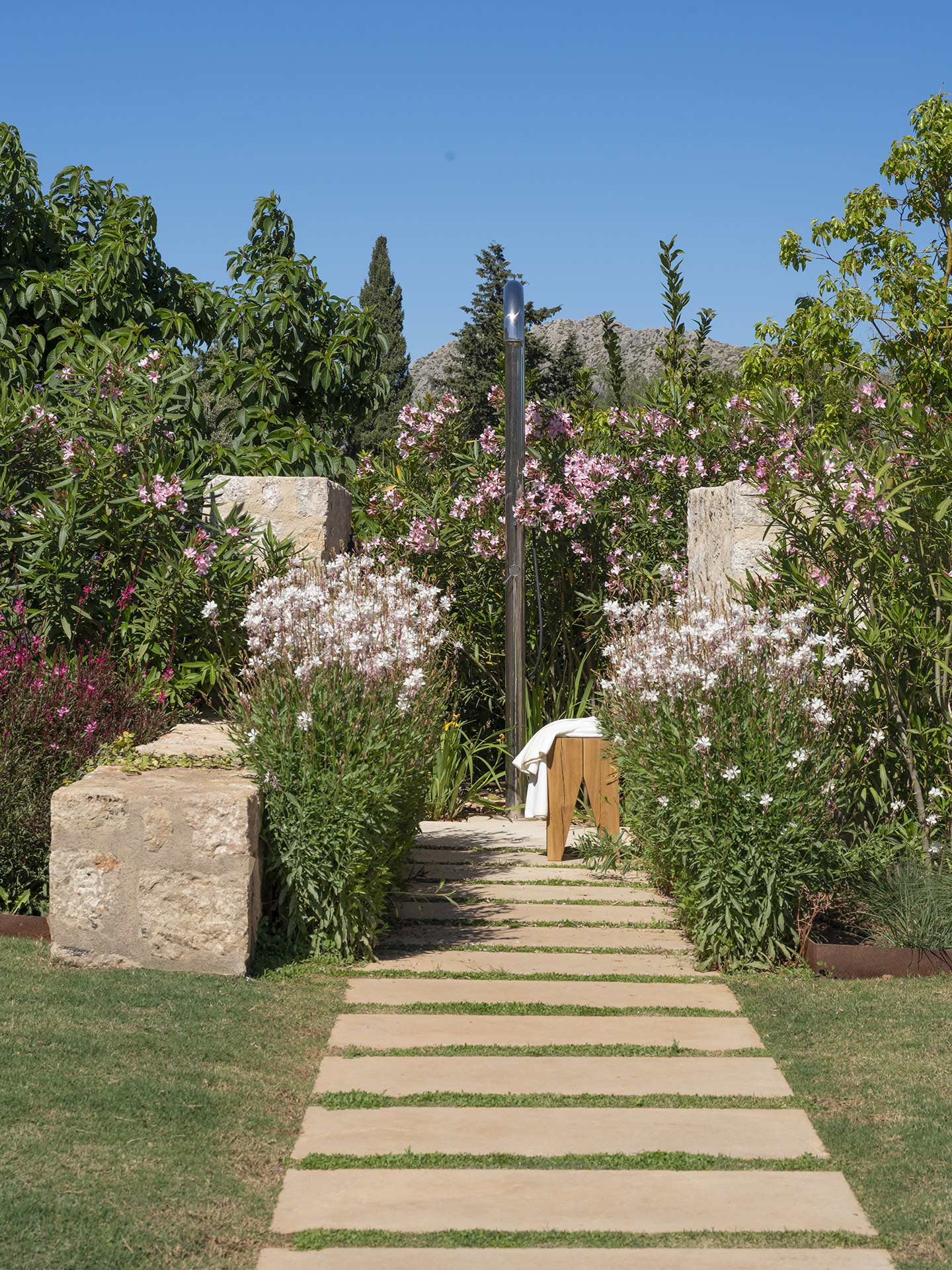 Camino de losas de piedra entre flores rosas y blancas que conduce a una ducha exterior