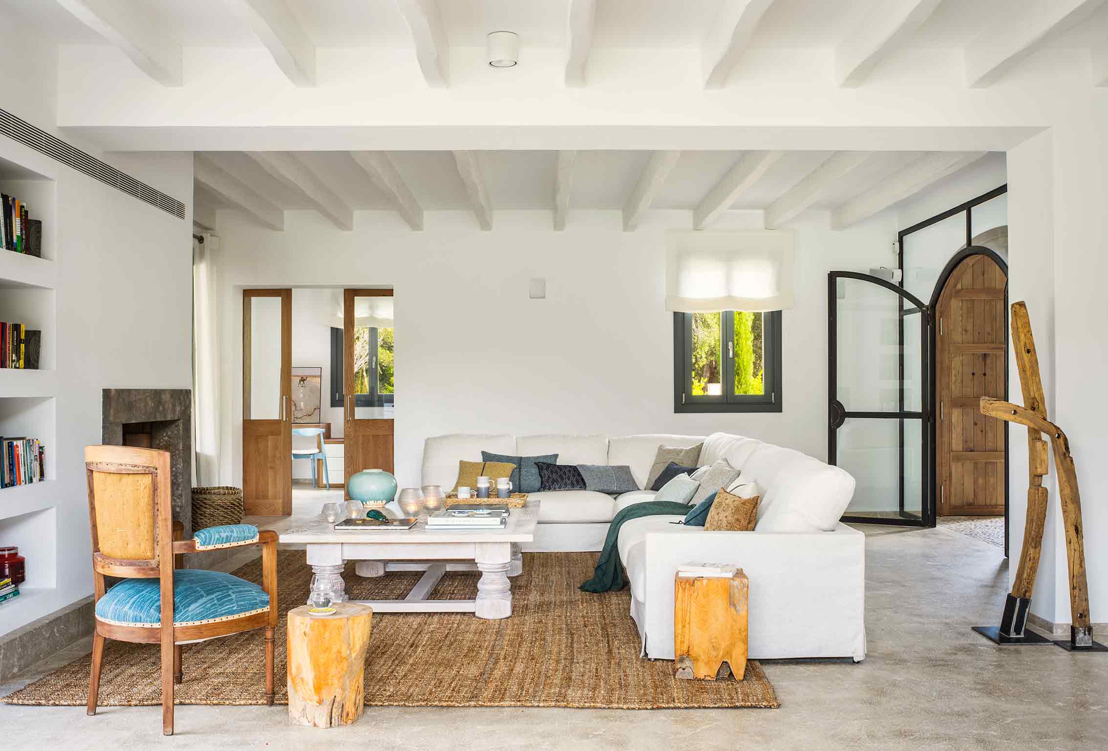 Heller mediterraner Wohnraum mit weißen Balken, Ecksofa, Jute-Teppich und Holztür mit Bogen