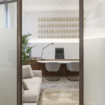 Von oxidiertem Stahl eingerahmtes Büro mit Holzschreibtisch, grauen Stühlen, hellem Sofa, Palme und Regalen