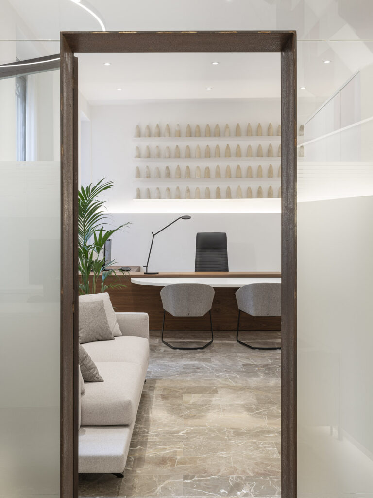 Von oxidiertem Stahl eingerahmtes Büro mit Holzschreibtisch, grauen Stühlen, hellem Sofa, Palme und Regalen