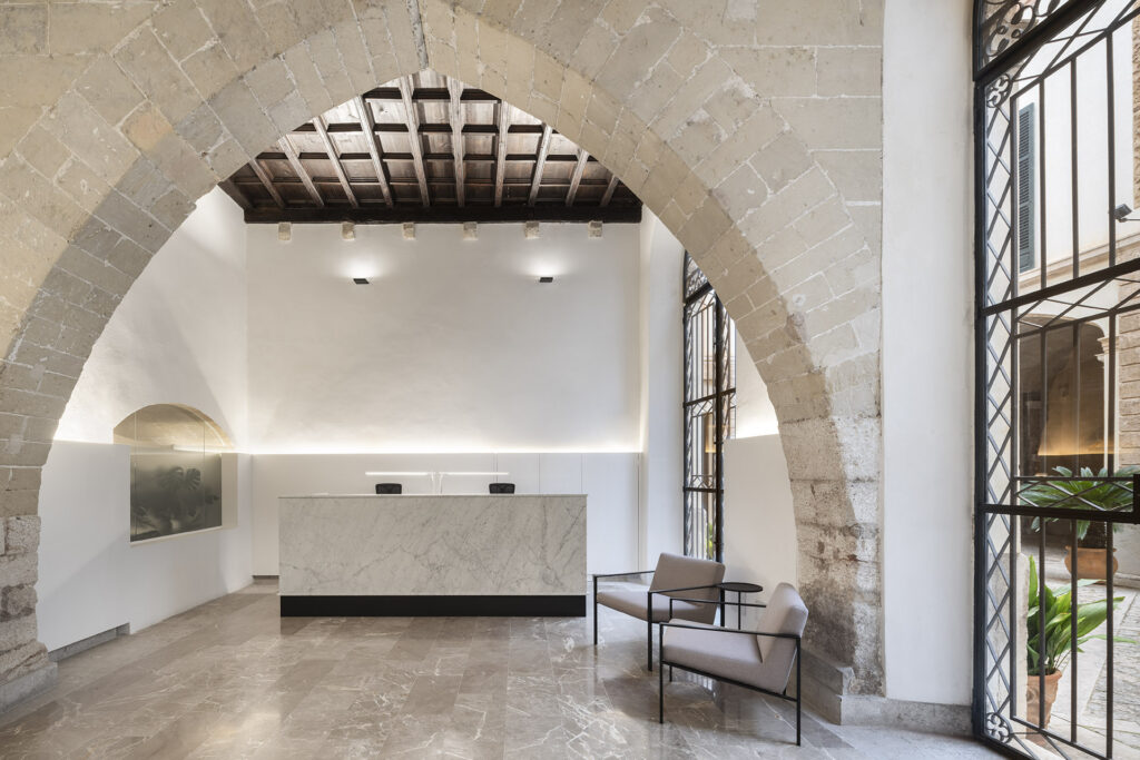 Recepción del Bufete Montis con arco de piedra, mostrador de mármol blanco y techo de vigas de madera