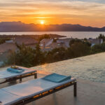 Sunset over the sea and mountains from the terrace, with sun loungers and an infinity pool