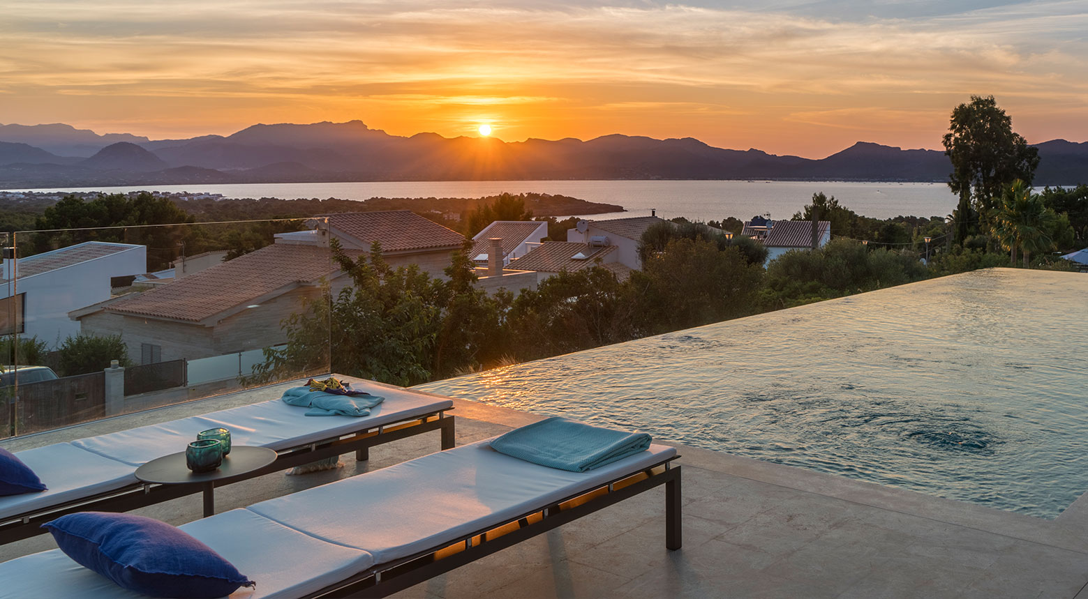 Sunset over the sea and mountains from the terrace, with sun loungers and an infinity pool