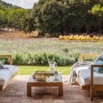Porche con sofás de madera, cojines azules, suelo de barro cocido y campo de lavanda al fondo