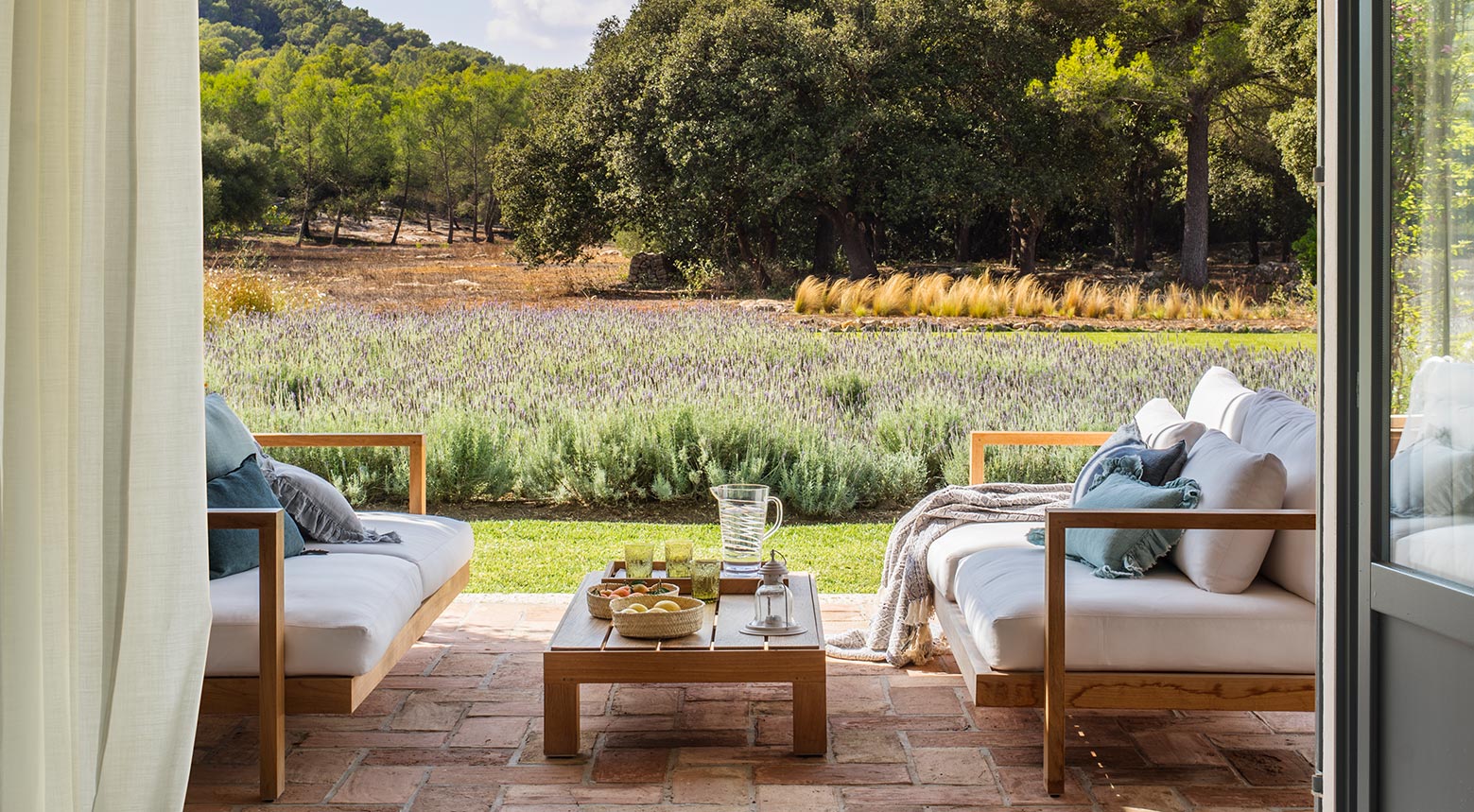 Porche con sofás de madera, cojines azules, suelo de barro cocido y campo de lavanda al fondo
