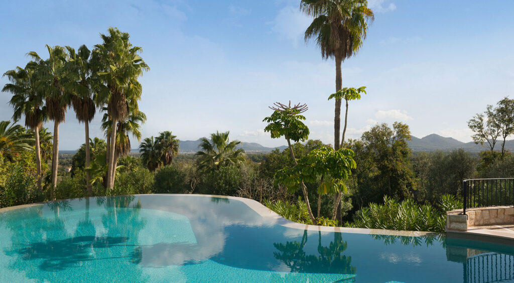 Borde infinito de la piscina con vistas a palmeras, campo y montañas al fondo