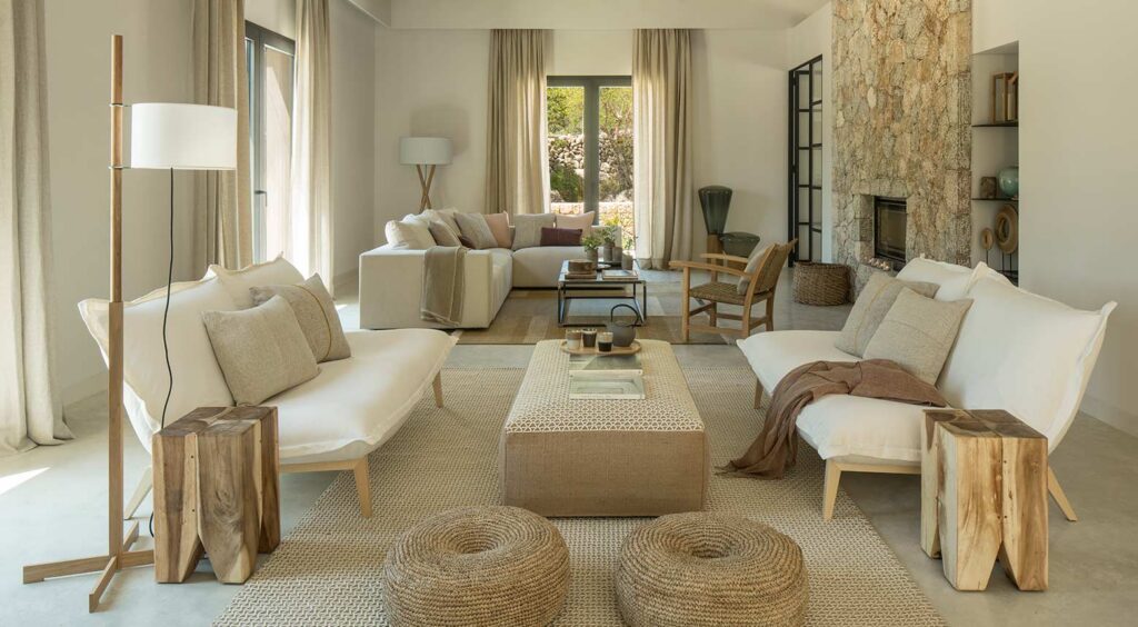 Helles Wohnzimmer mit weißen Sofas, Steinkamin, beigen Vorhängen und Beistelltischen aus Holz