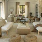 Helles Wohnzimmer mit weißen Sofas, Steinkamin, beigen Vorhängen und Beistelltischen aus Holz