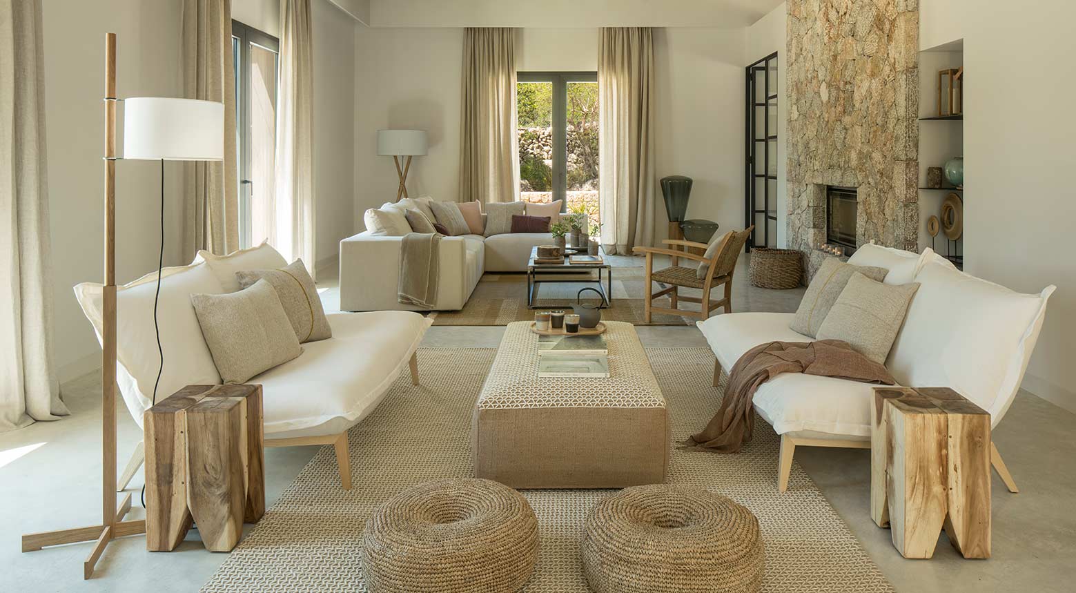 Helles Wohnzimmer mit weißen Sofas, Steinkamin, beigen Vorhängen und Beistelltischen aus Holz