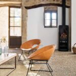 Wohnzimmer mit Kieselsteinboden, Ledersesseln, schwarzem Kaminofen und Metalltreppe