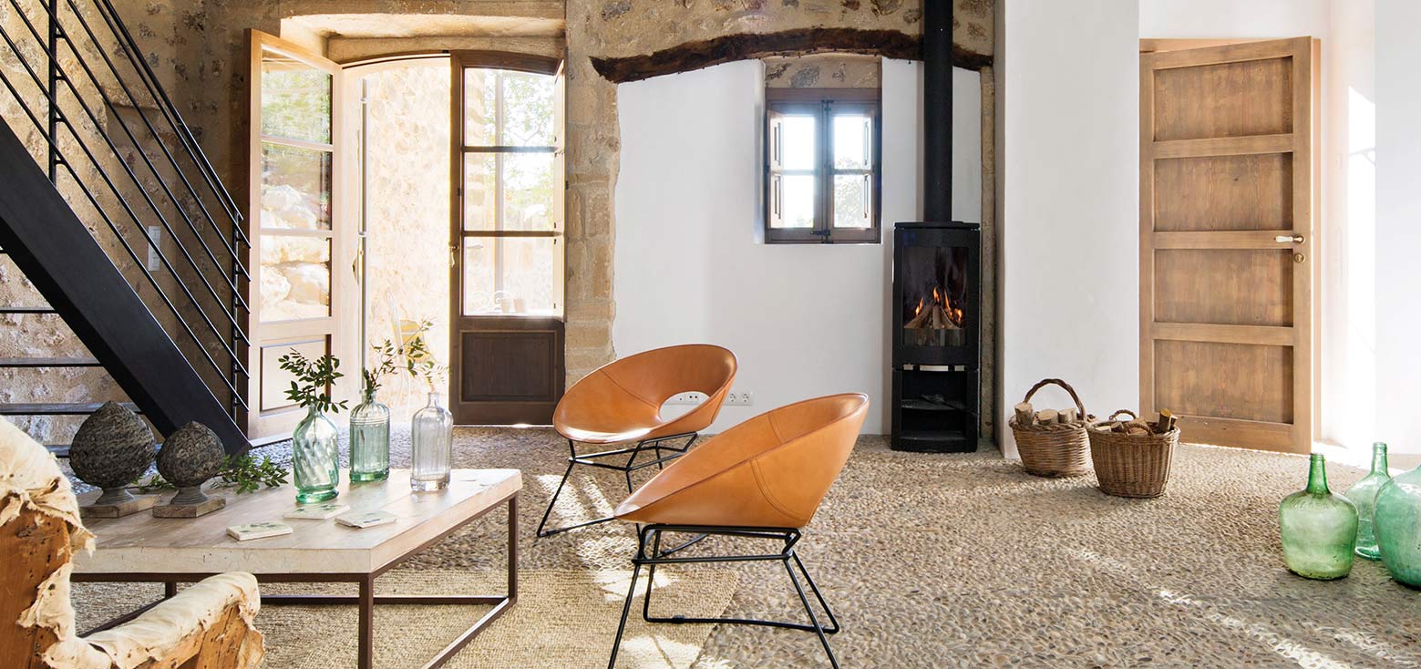 Wohnzimmer mit Kieselsteinboden, Ledersesseln, schwarzem Kaminofen und Metalltreppe