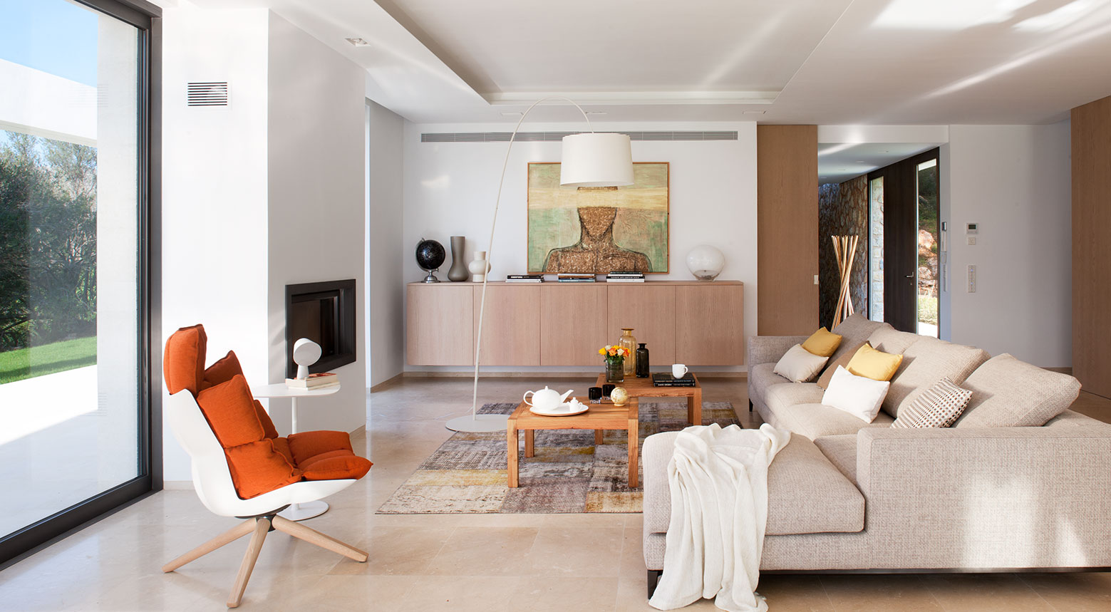 Salón luminoso con sofá beige, sillón naranja, aparador de madera clara, chimenea y suelo pulido claro