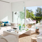 Helles Wohnzimmer mit cremefarbenem Sofa, weißem Tisch und Juteteppich, offen zu Terrasse und Garten