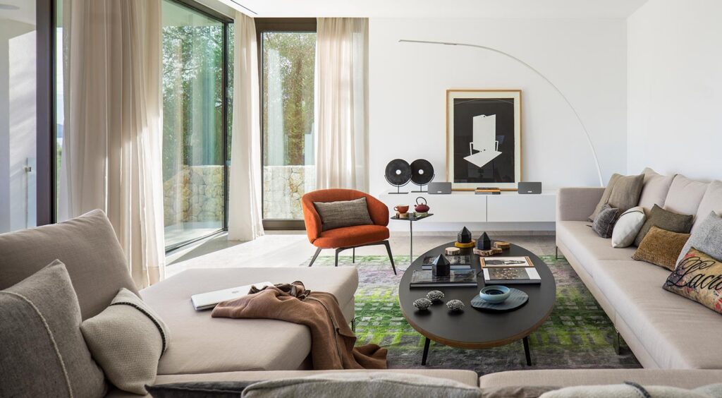 Salón con sofás beige, butaca naranja, alfombra verde, cortinas ligeras y cuadro en blanco y negro
