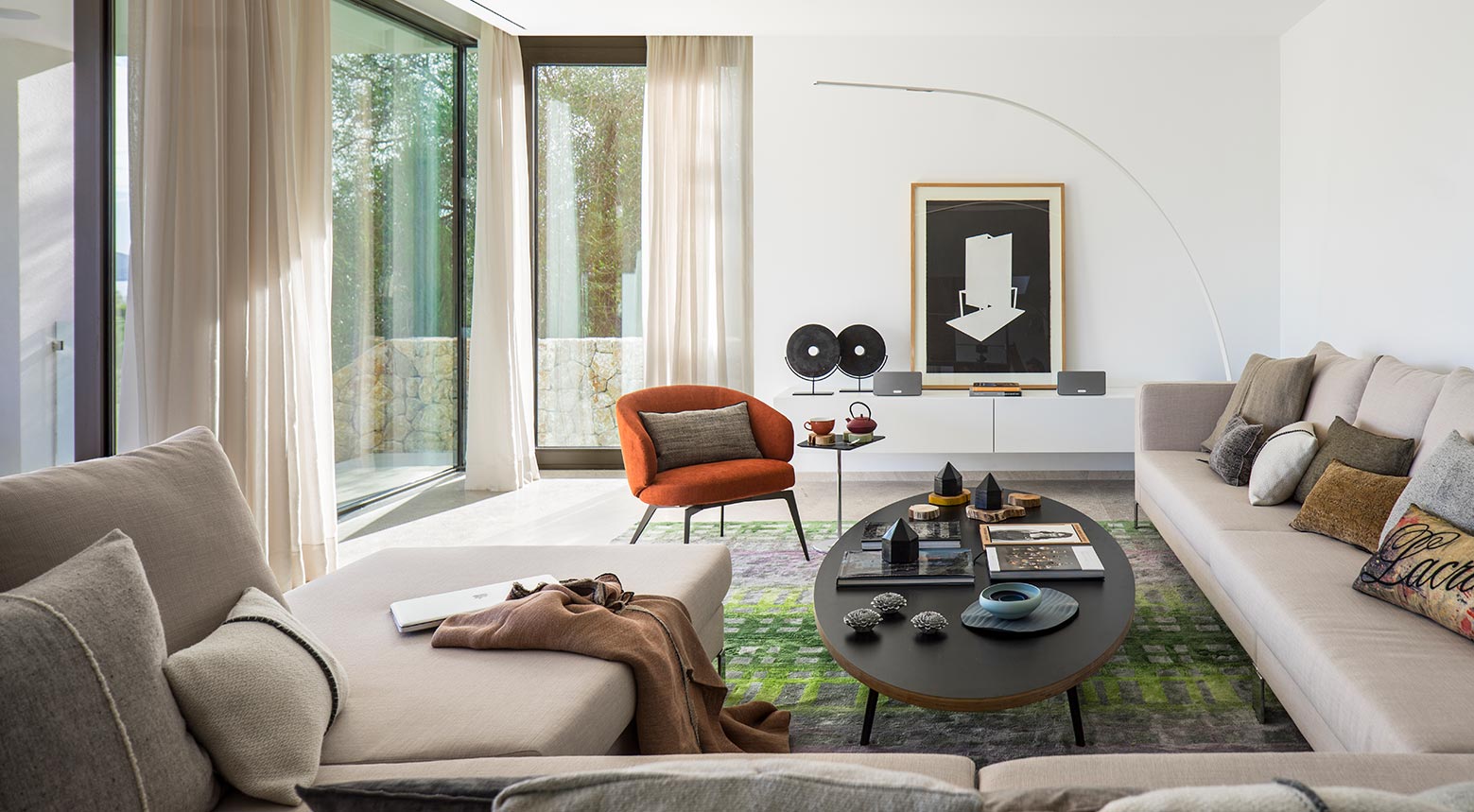 Salón con sofás beige, butaca naranja, alfombra verde, cortinas ligeras y cuadro en blanco y negro