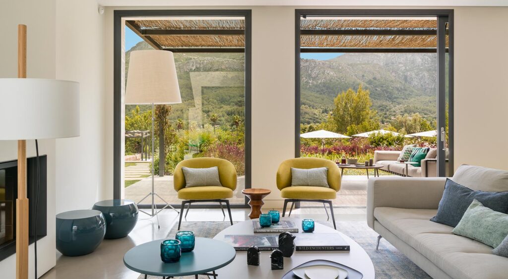Helles Wohnzimmer mit gelben Sesseln und großen Fenstern mit Berg- und Gartenblick