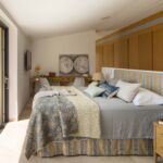 Dormitorio con cabecero rayado, armarios de madera y puerta corredera a un balcón con vistas.