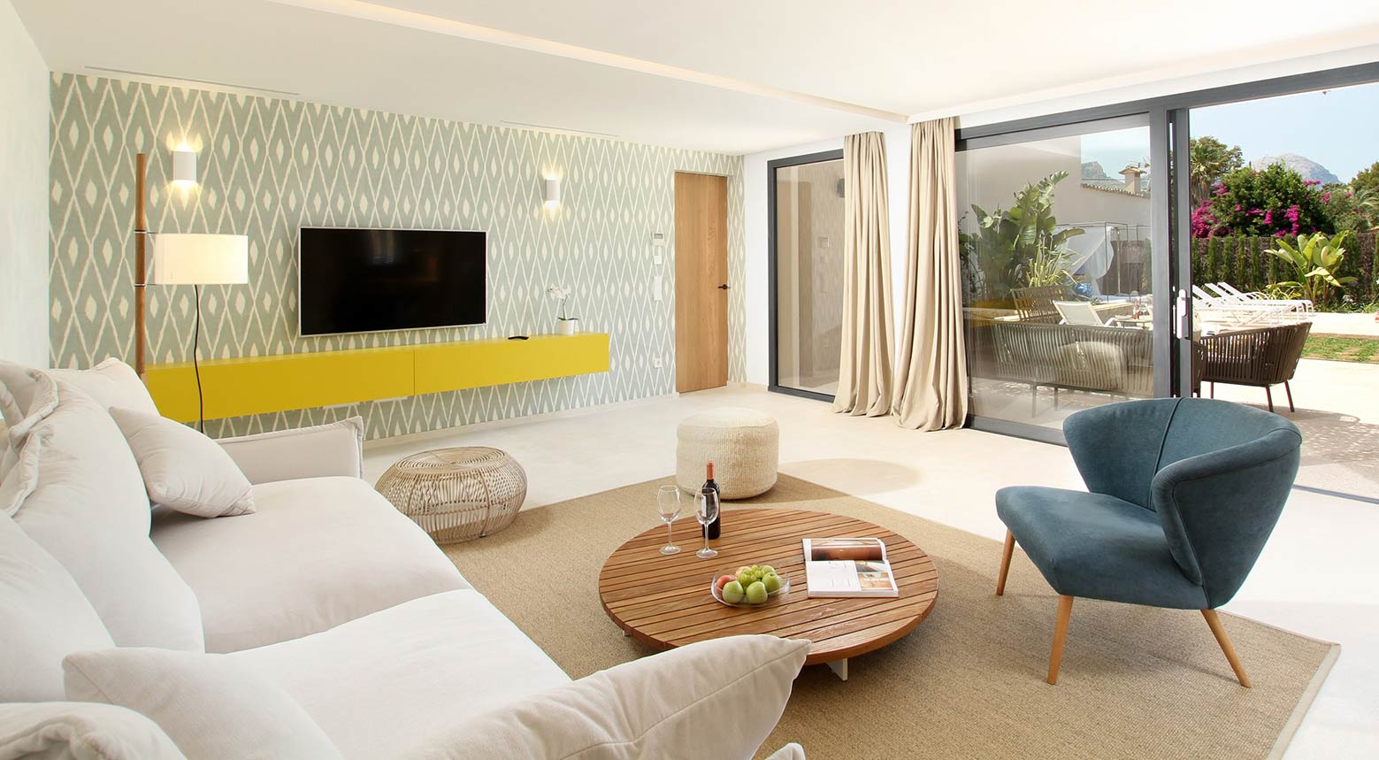 Salón con sofá blanco, sillón azul, mesa baja redonda de madera y mueble amarillo bajo la televisión