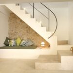 Escalera blanca con banco y cojines verdes bajo pared de piedra vista, con peldaños de piedra clara