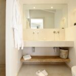 Baño con doble lavabo de piedra clara sobre balda de madera natural, gran espejo y ducha de microcemento