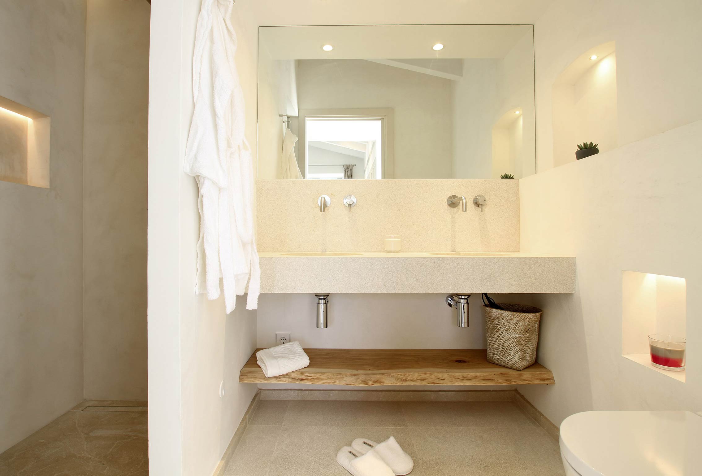 Baño con doble lavabo de piedra clara sobre balda de madera natural, gran espejo y ducha de microcemento