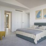 Dormitorio en otro ángulo con armarios blancos empotrados, cuadros azules sobre beige y puerta al baño
