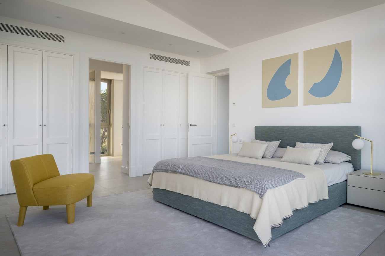 Dormitorio en otro ángulo con armarios blancos empotrados, cuadros azules sobre beige y puerta al baño