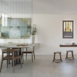 Comedor con sillas de madera visto a través de un cristal, con la cocina y taburetes al fondo
