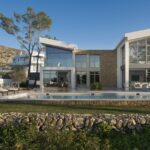 Fachada de la villa con piscina, muro de piedra seca en primer plano y montaña detrás
