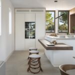 Cocina blanca con isla y barra volada de madera de nogal, taburetes y electrodomésticos integrados