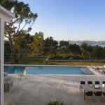 Terraza con piscina, comedor exterior y tumbonas vistos desde un nivel elevado, con el mar al fondo
