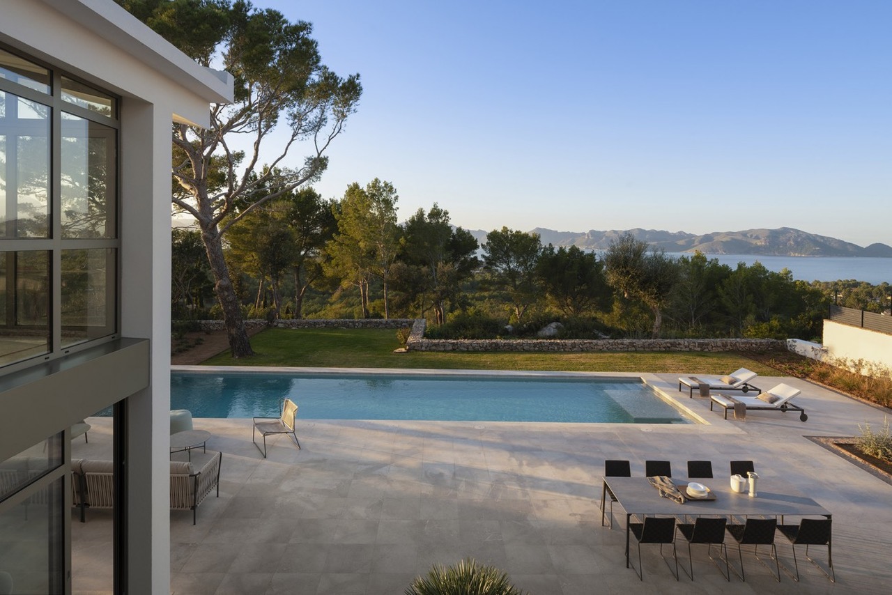 Terraza con piscina, comedor exterior y tumbonas vistos desde un nivel elevado, con el mar al fondo