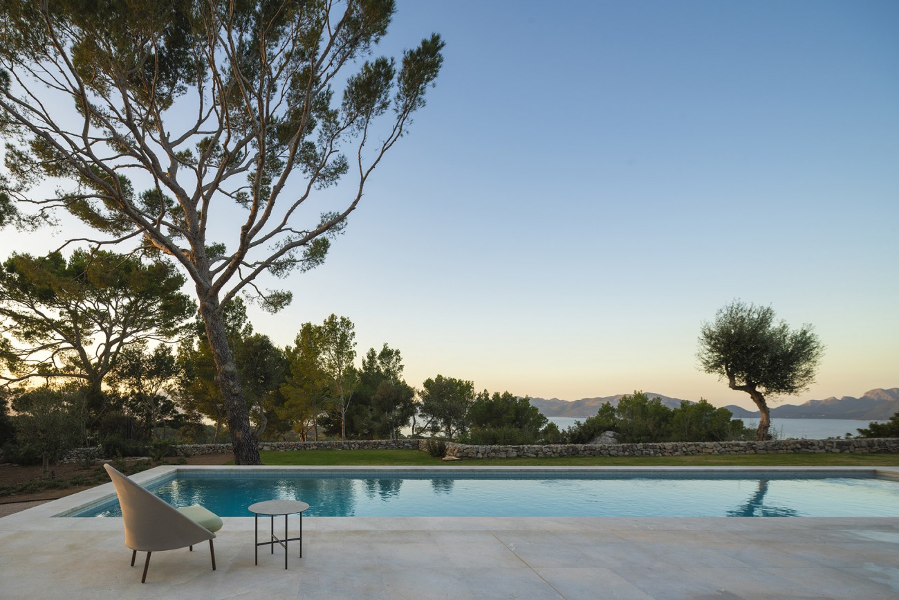 Piscina al atardecer con pino, muro de piedra seca y vistas al mar y a la montaña