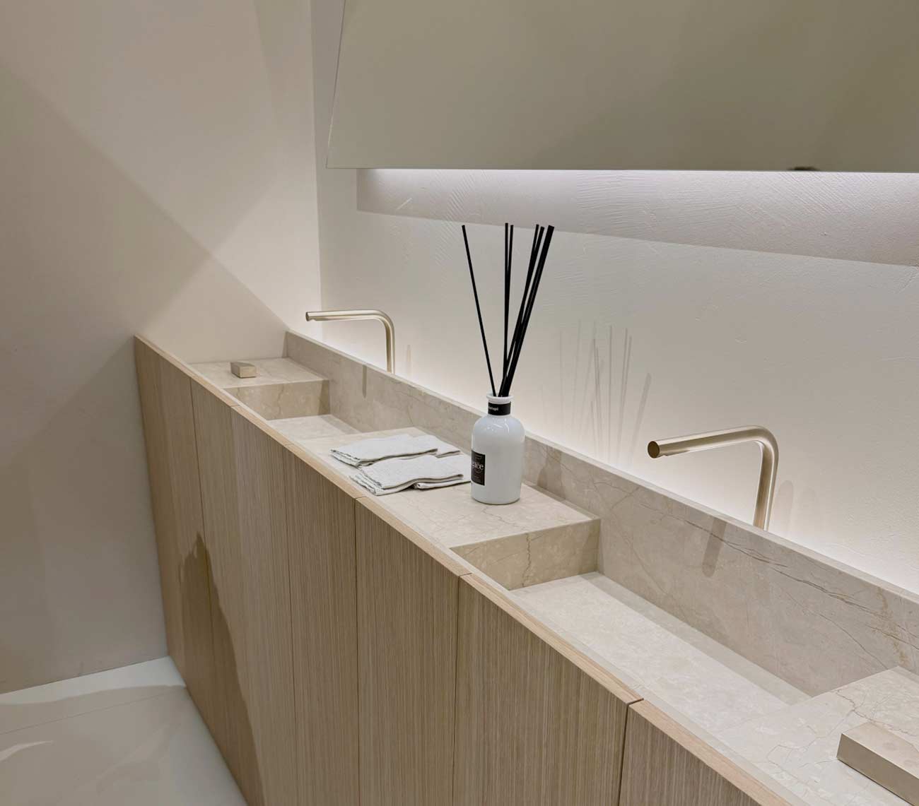 Helle Steinplatte mit integrierten Waschbecken, Holzmöbeln und matter goldener Armatur