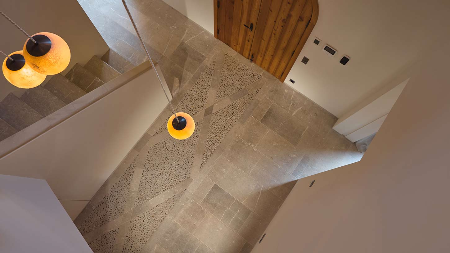 Draufsicht auf einen Eingangsbereich mit Steinboden und Kieselmosaik, Treppe und Hängeleuchten