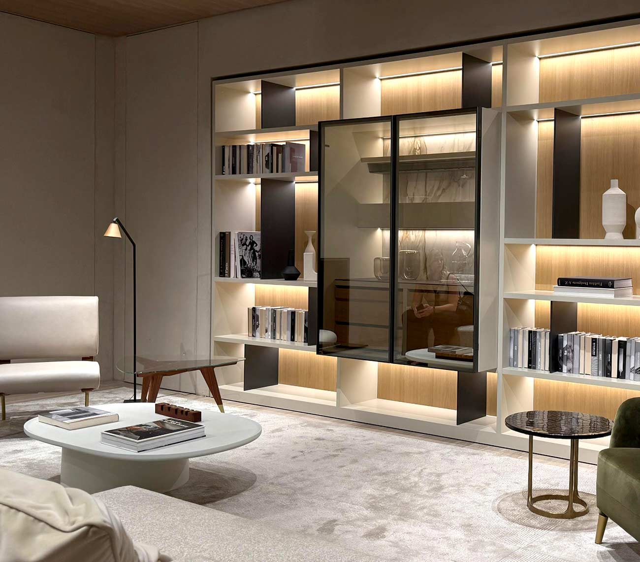 Wohnzimmer mit beleuchtetem Holzregal und Vitrine aus Rauchglas, weißem Couchtisch und grünem Sessel