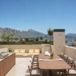 Cubierta de día con comedor de madera, tumbonas de rayas amarillas, barbacoa y vistas a montañas y mar