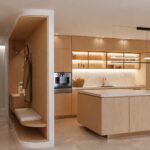 Entrada con hornacina curva de roble con banco y abrigo colgado junto a la cocina abierta