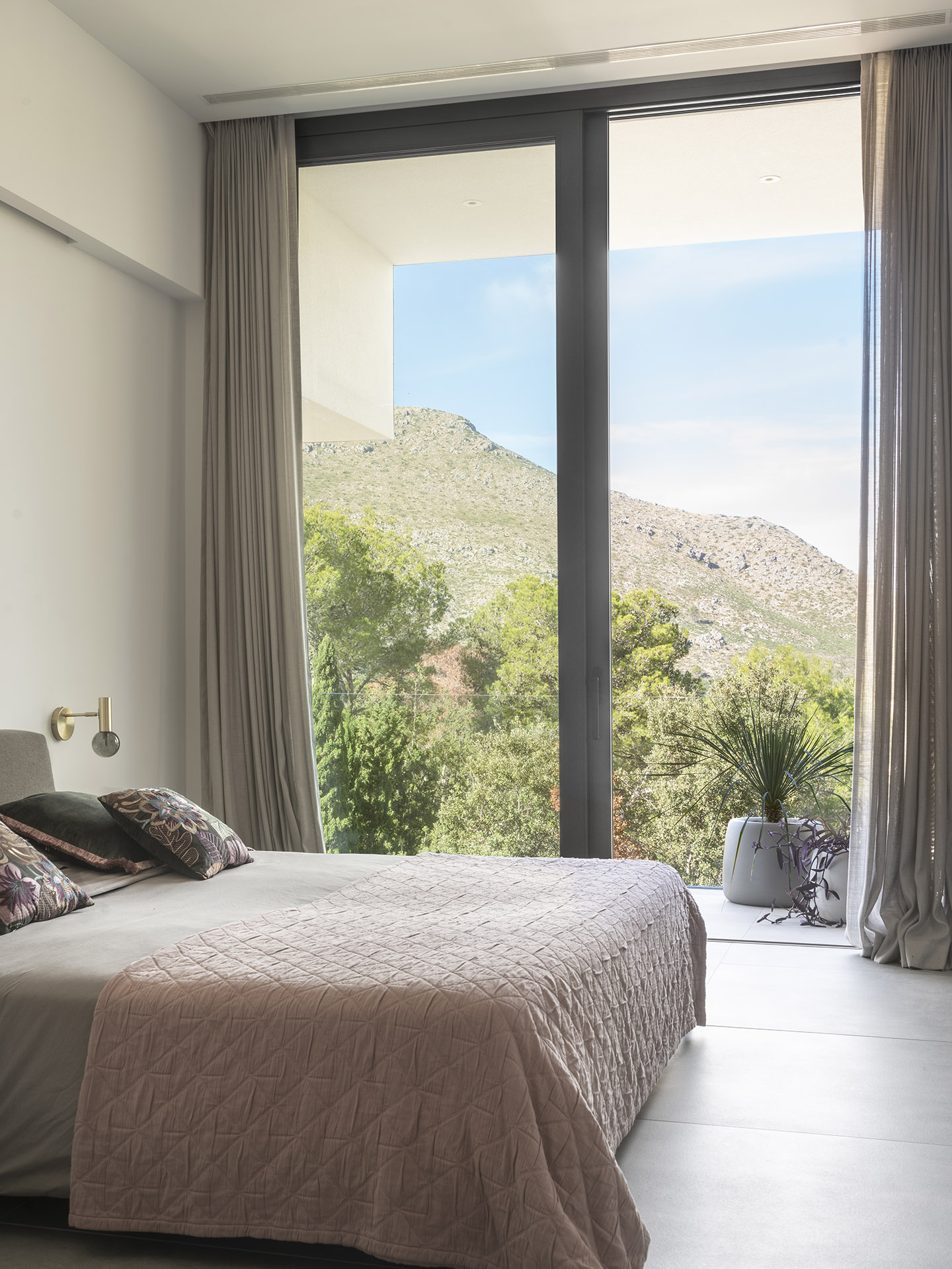 Dormitorio con ventanal de suelo a techo, cortinas de lino y vistas a la montaña entre pinos