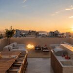Cubierta con comedor de madera, zona chill out, barbacoa y puesta de sol sobre tejados y mar