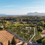 Vista aérea del entorno de Can Melis con arbolado, campos, el mar y las montañas al fondo