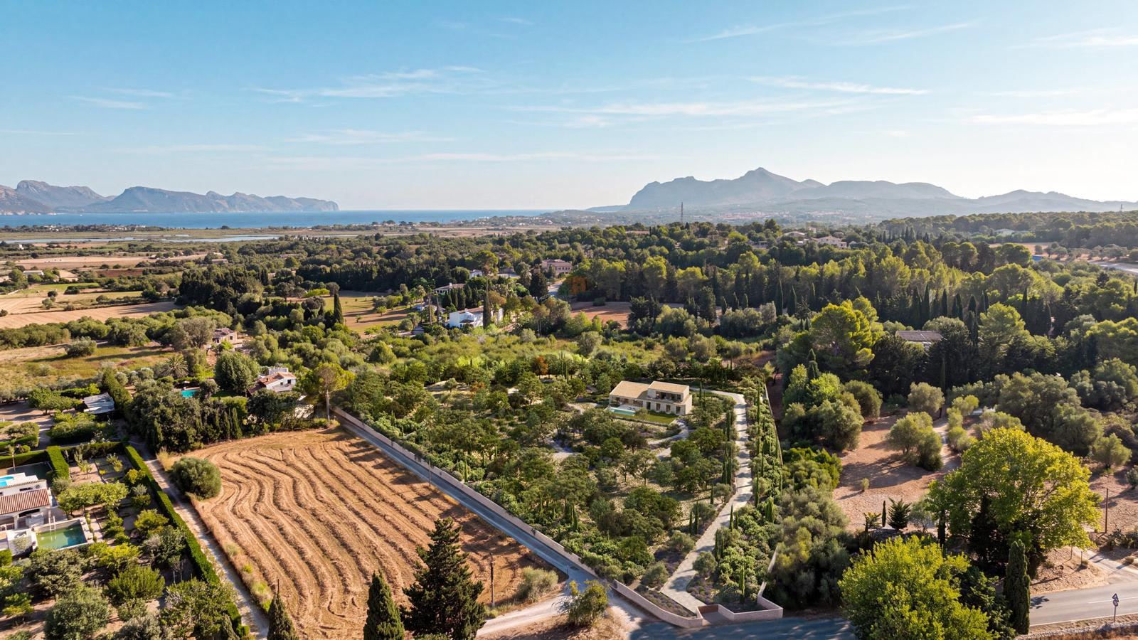 Vista aérea del entorno de Can Melis con arbolado, campos, el mar y las montañas al fondo