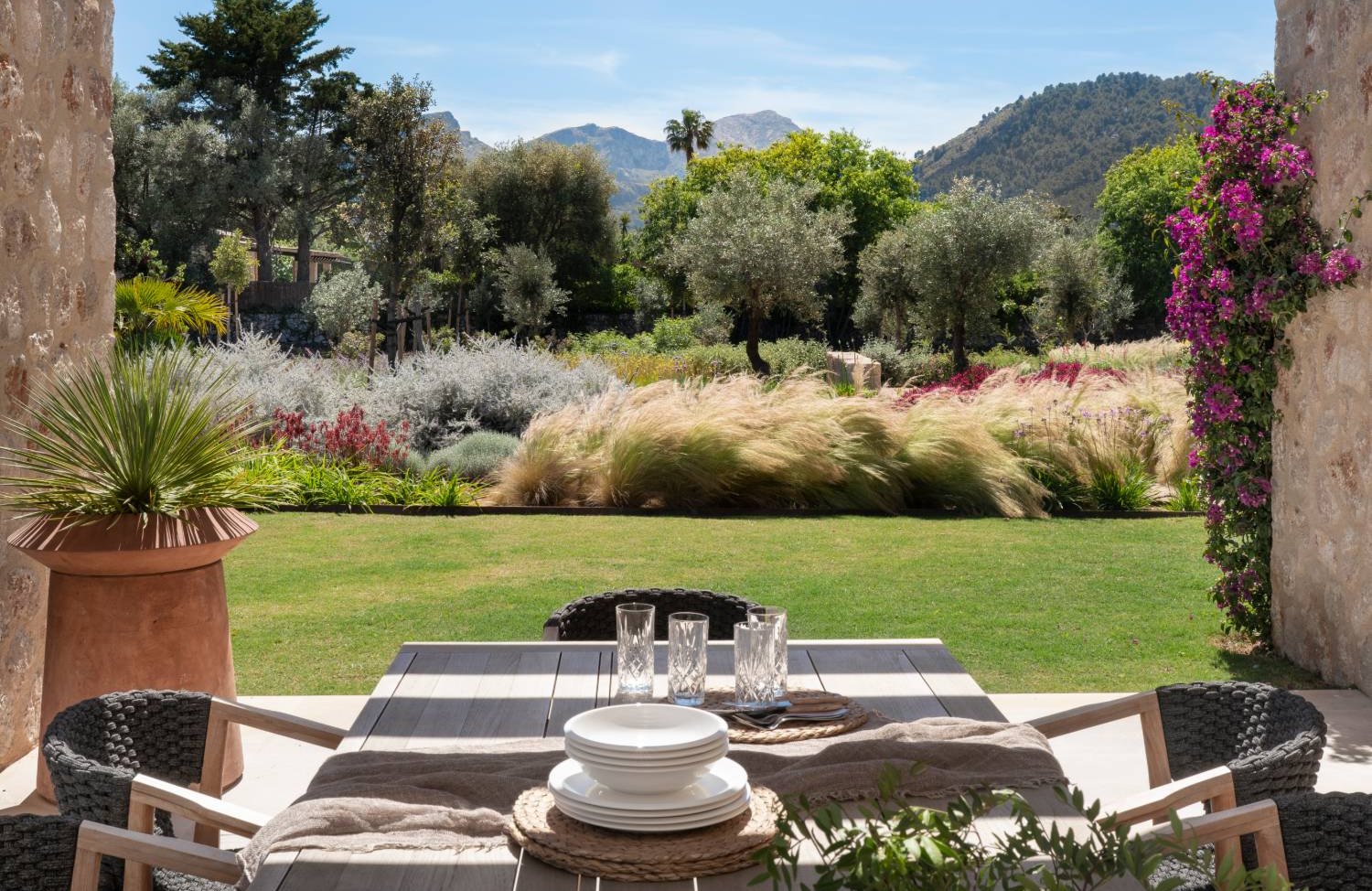 Comedor exterior bajo la pérgola con vistas al jardín mediterráneo, la bugambilia y la sierra